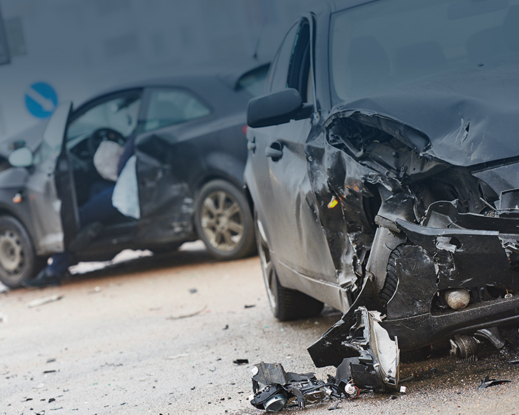 Crashed black car with significant frontal damage and debris scattered around, highlighting the aftermath of a severe vehicle accident.